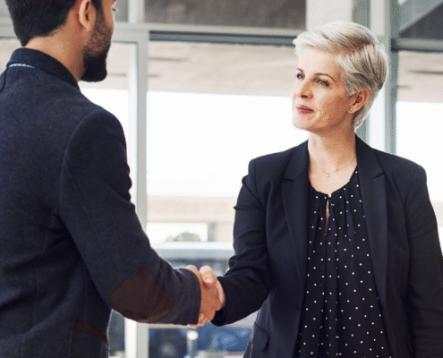 Professional woman in black blazer shaking hands with man in business suit during job offer negotiation meeting in modern office